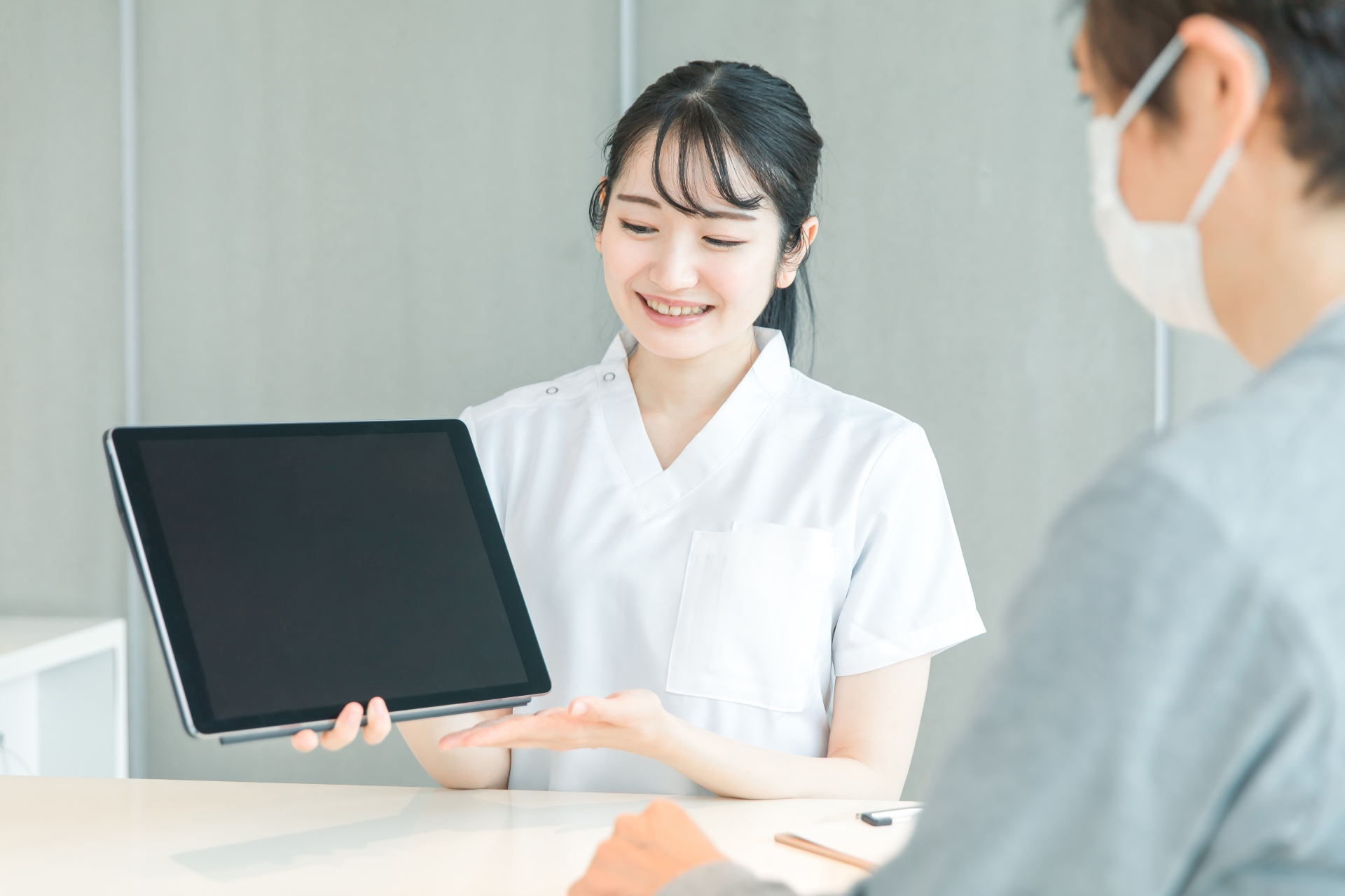 タブレットPCで受付する白衣の女性と患者